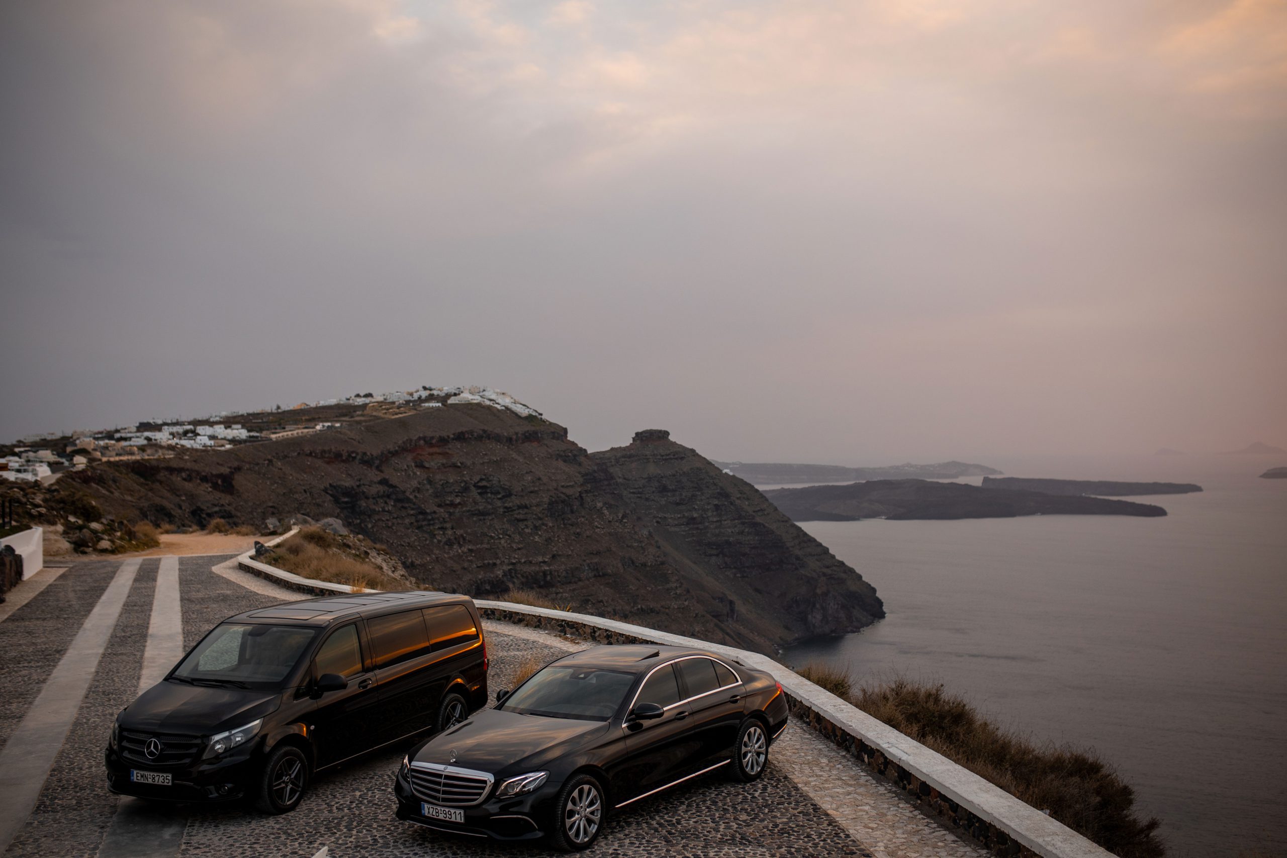 Mercedes-Benz Vito van and E-Class on a clifftop overlooking the Santorini caldera at dusk