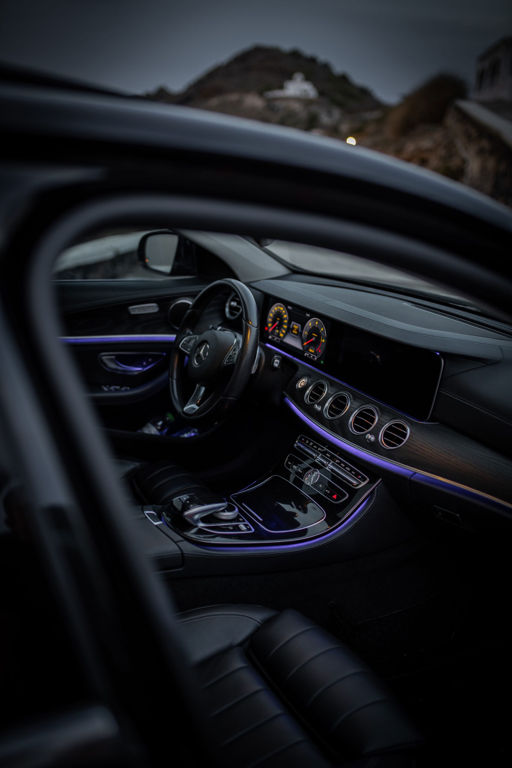 Illuminated dashboard and steering wheel of a Mercedes-Benz E-Class with a Santorini chapel beyond