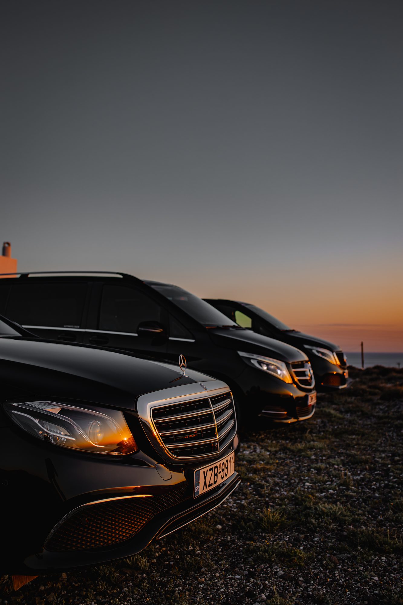 Row of black Mercedes-Benz vehicles parked on a Santorini clifftop at twilight