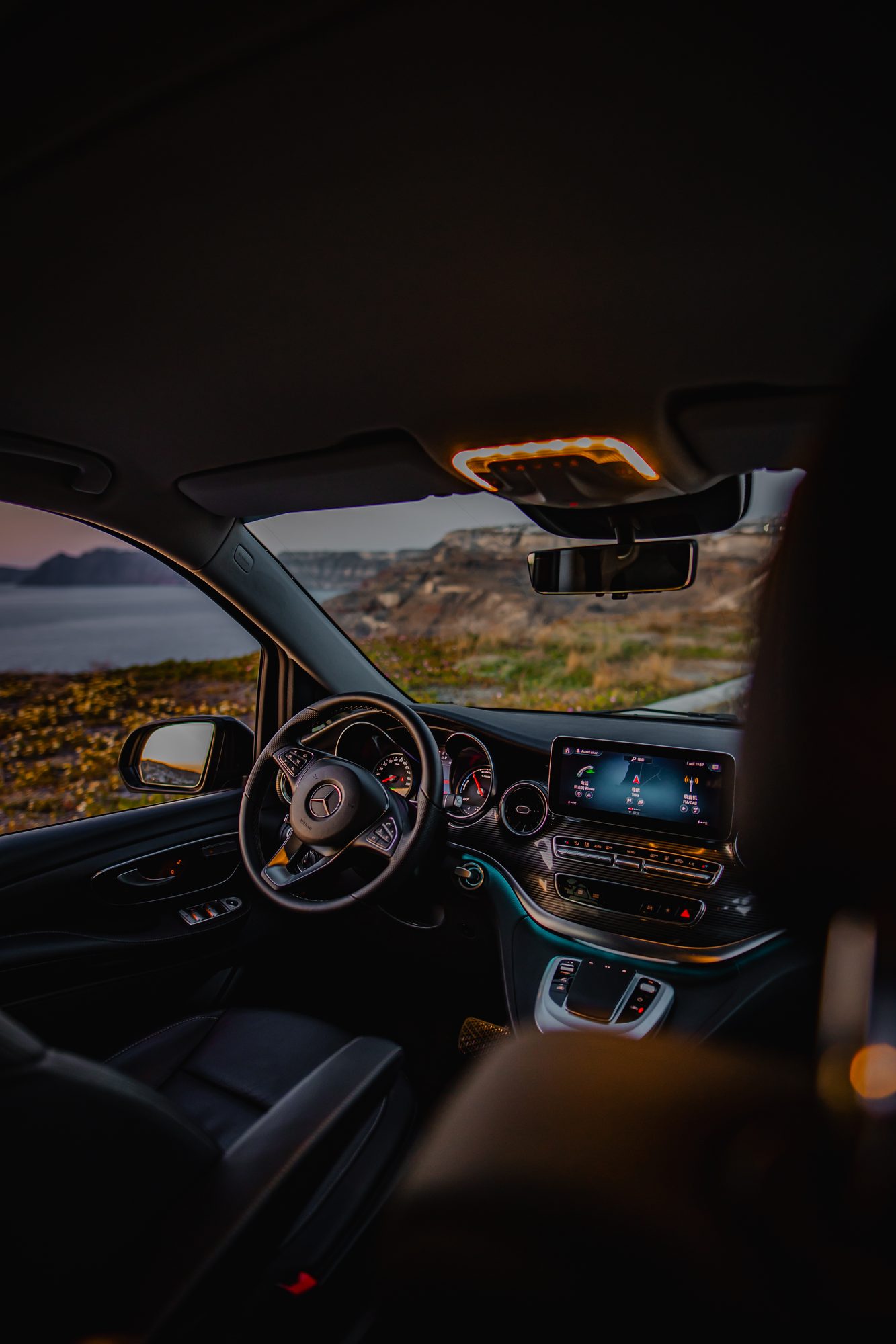 Driver's view from a Mercedes-Benz cockpit overlooking the Santorini coastline at dusk