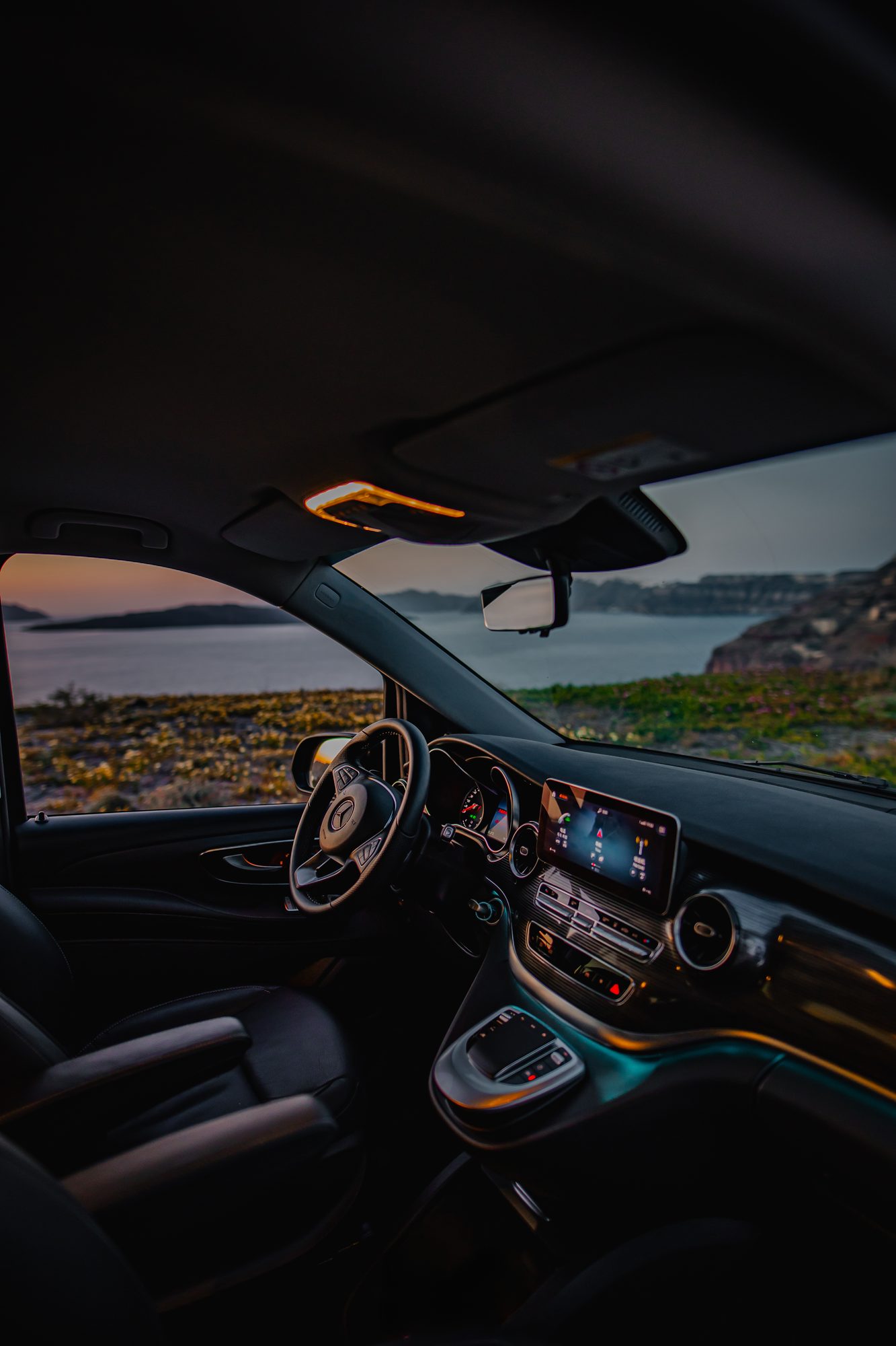 Steering wheel and digital dashboard of a Mercedes-Benz van facing the Santorini sea at dusk