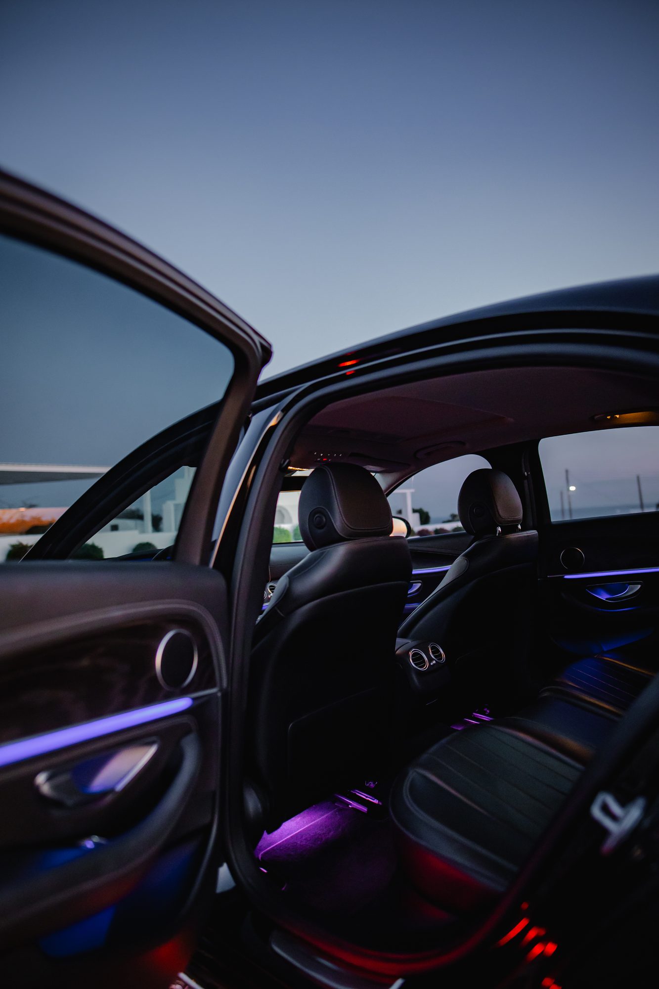 Open door of a Mercedes-Benz revealing ambient-lit leather seats at twilight in Santorini